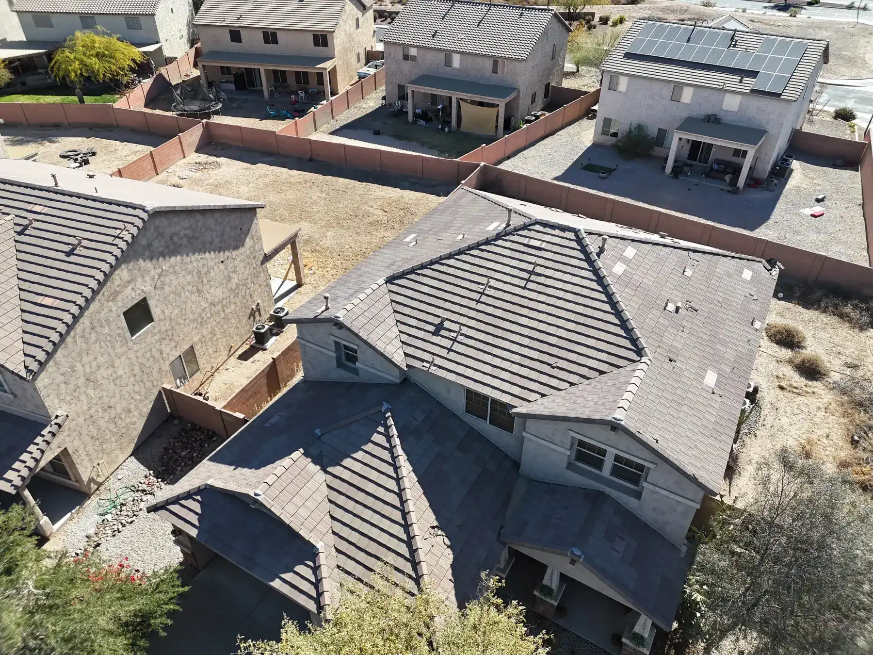 High oblique view of gray tile roofs with polygonal hips beside a gravel yard