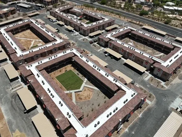 Oblique aerial view of brown pitched roofs and white low-slope sections enclosing landscaped courtyards