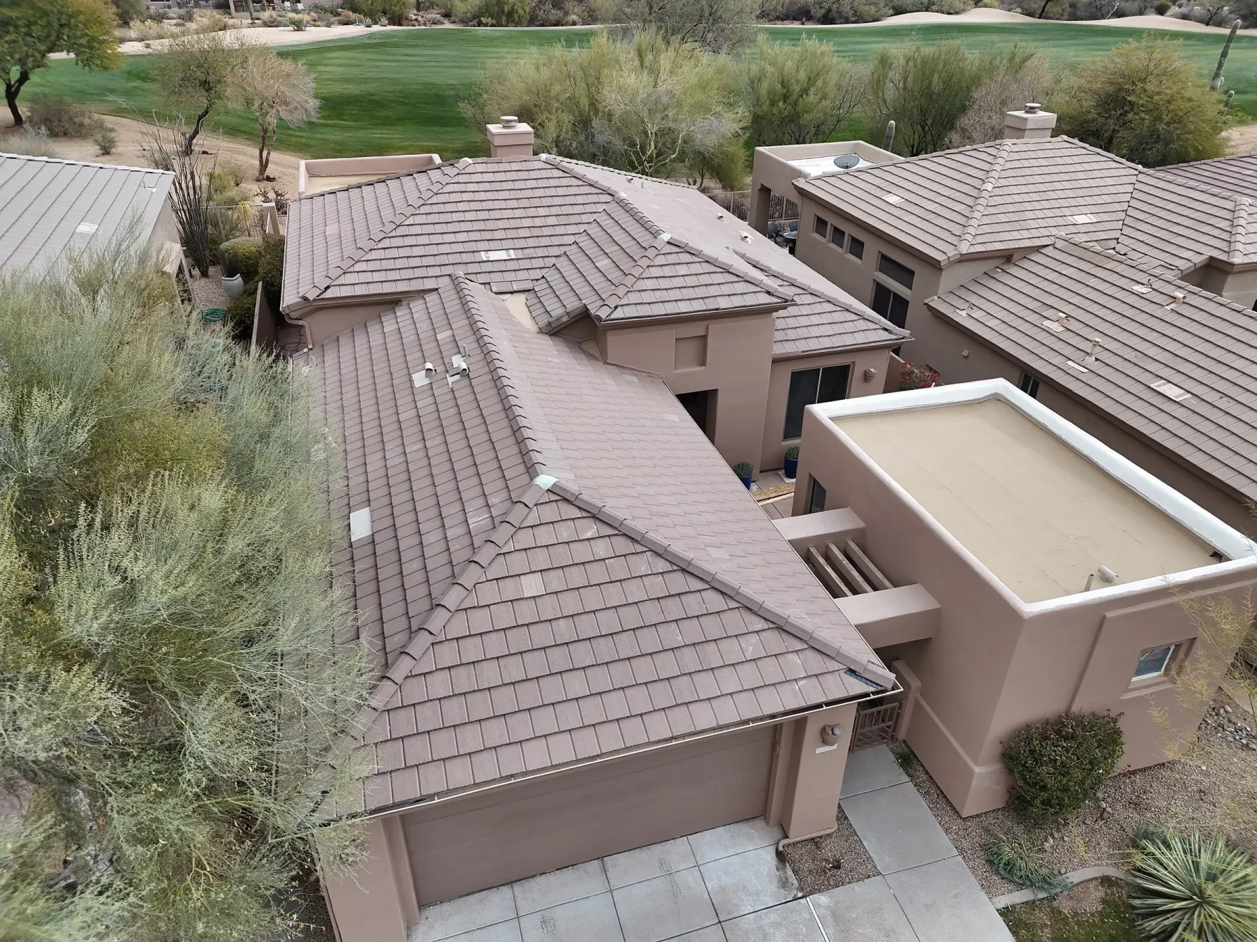 Oblique aerial view of tan tile roofs across closely spaced homes with angular garages