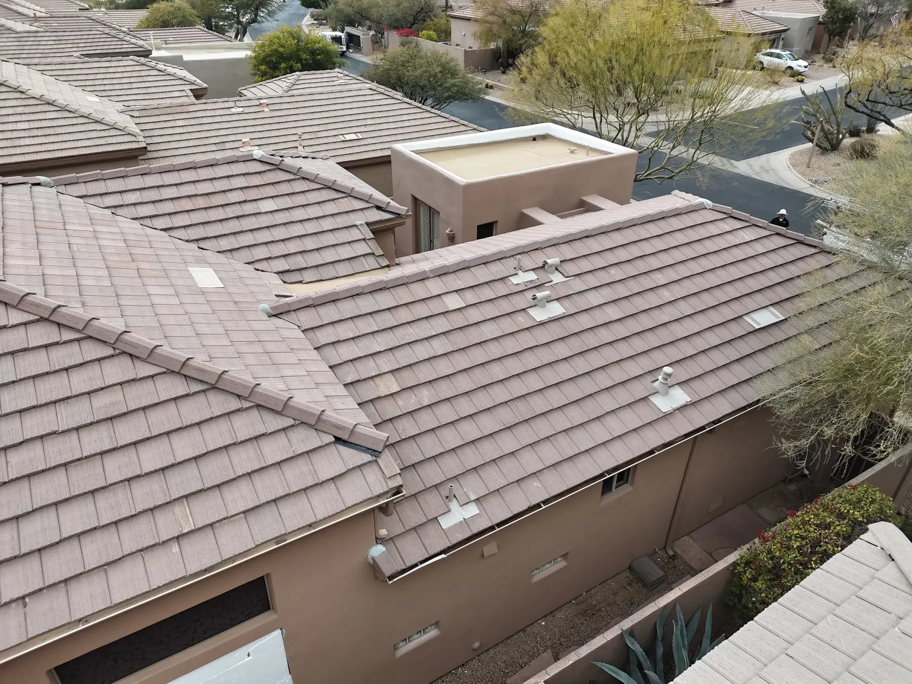 Close oblique view of brown tile roofing with intersecting hips, vents, and tan parapets