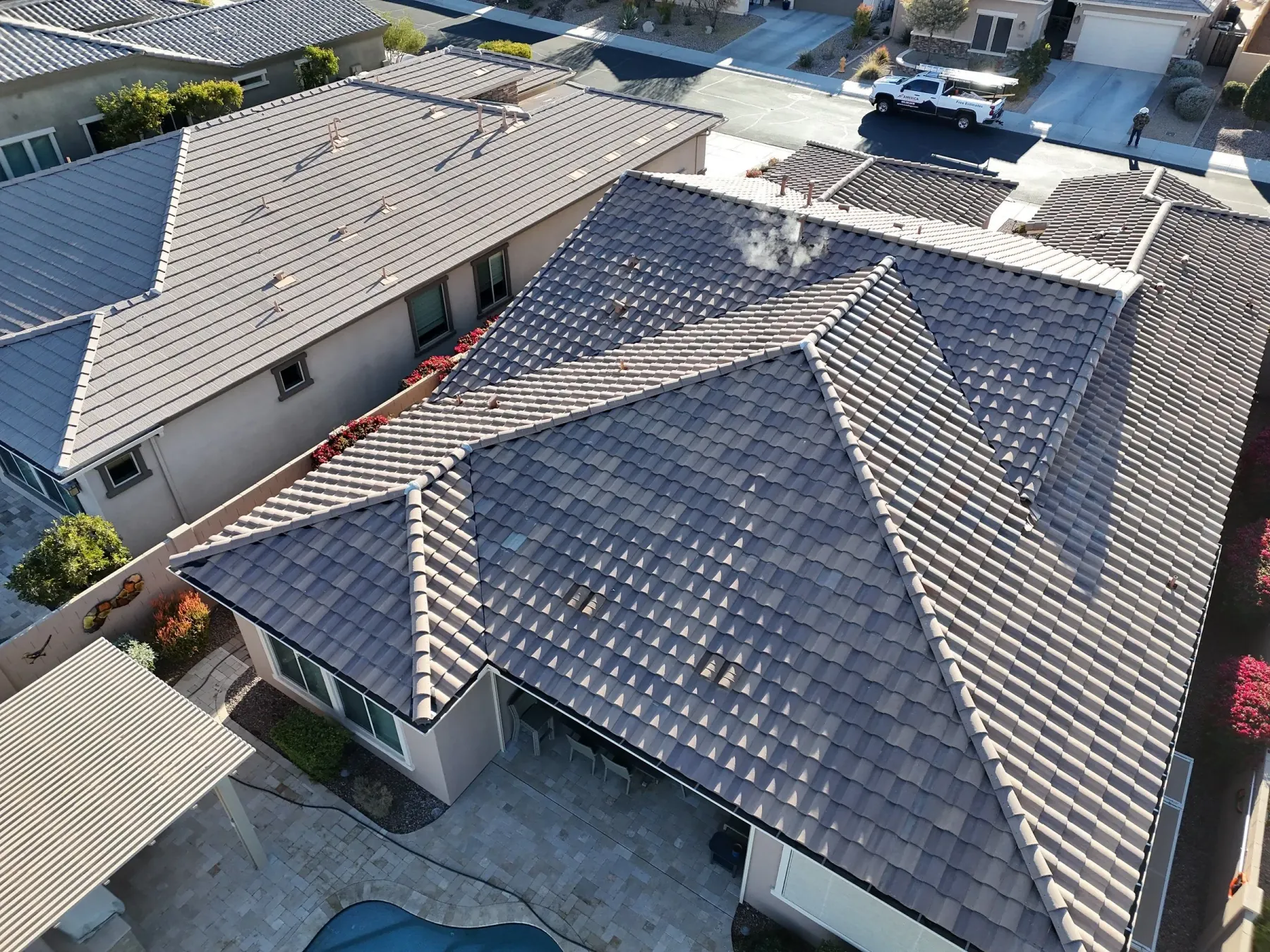 Oblique aerial view of blue-gray tile roofing with multiple hips beside a light gray roof
